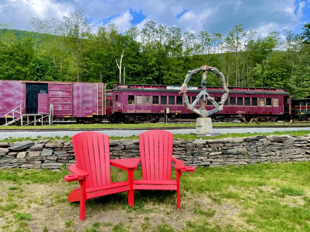Red Adirondack chairs in front of an old train in Ulster County, NY
